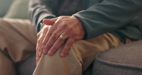 Senior's Hands Clasped Over Knee Sitting on Sofa