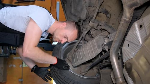 Auto Mechanic Working on Vehicle in Garage Underneath Car