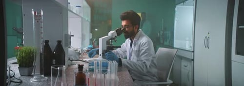 Scientist Working With Microscope in Bright Lab
