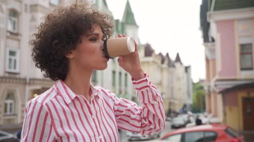 Happy young woman enjoying takeout coffee on urban city street in europe