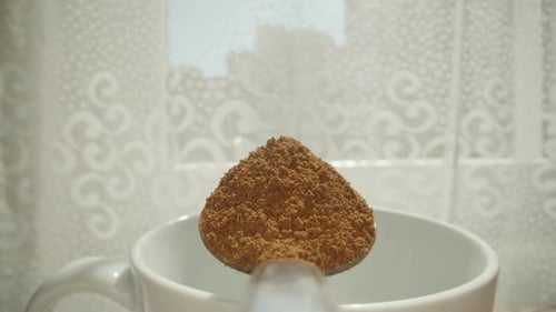 I put the mug down and pour instant coffee into it with a spoon. Dolly slider extreme close-up.