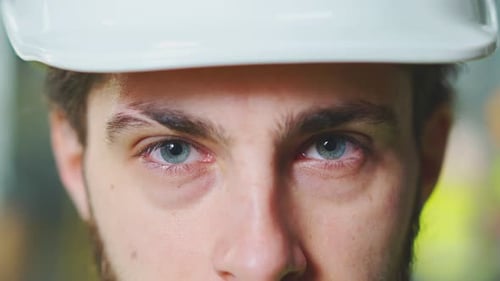 Nahaufnahme eines kaukasischen jungen männlichen Ingenieurs mit weißem Helm, der direkt in die Kamera schaut