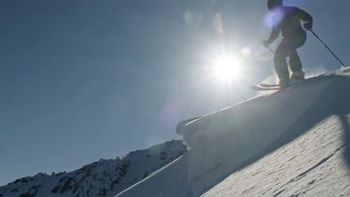 Professional Skier Jumping From Snowy Mountain Ridge in Bright Sunlight