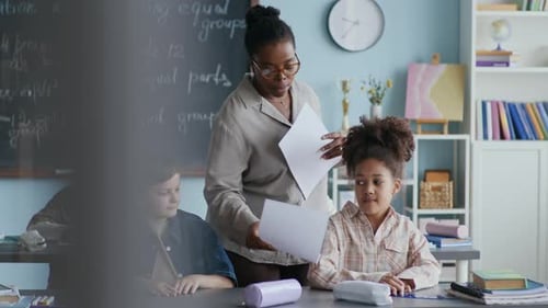 Teacher Reviews Elementary Students' Work in Classroom