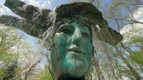 Сamera moves close to water jets from bronze mask fountain, slow motion