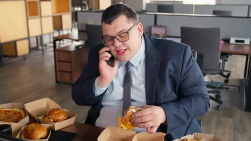 Overweight Man Eats Fast Food at Office Desk