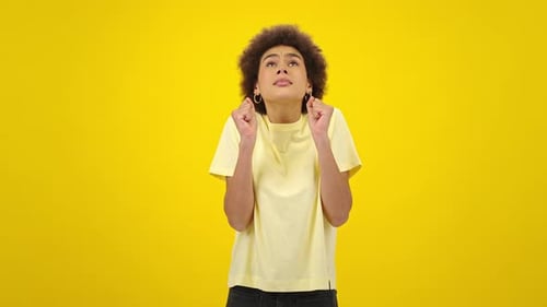 Woman Pleading, Making a Wish on Yellow Background