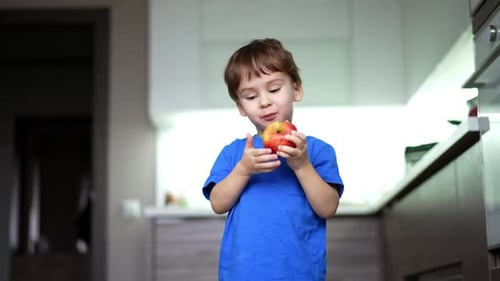Happy Boy Eating a Delicious Apple in Kitchen