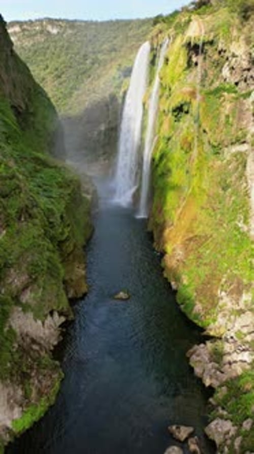 Aerial drone view of Tamul Waterfall cascading down green cliffs into a turquoise pool below. Vertic