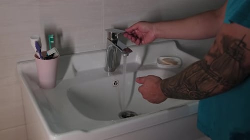 Morning hygiene man with tattoos wash his hands and face, not forgetting to turn off the faucet