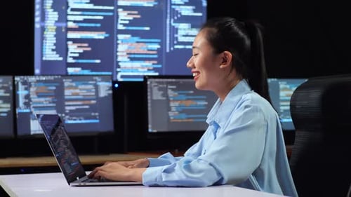 Vue latérale d'une programmeuse asiatique écrivant du code par un ordinateur portable à l'aide de plusieurs moniteurs