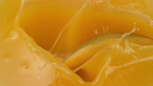 Mango slices dropped into yellow juice in slow motion