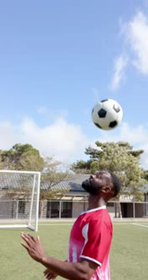 Vertical video: Soccer player in red jersey heading ball on outdoor field, focused and determined