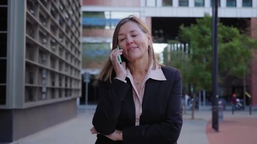 Smiling Businesswoman Using Smartphone Texting and Talking on the Phone in Urban City After Work