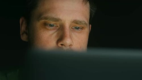Closeup of a Young Freelancer Working on a Laptop in the Evening The Programmer Focuses Intently on