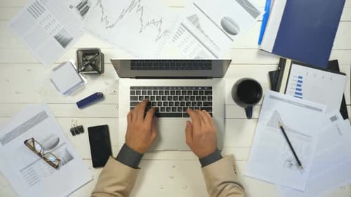 Male Arms of Businessman Typing Text on Laptop Keyboard at White Desk Top View Hands of Manager