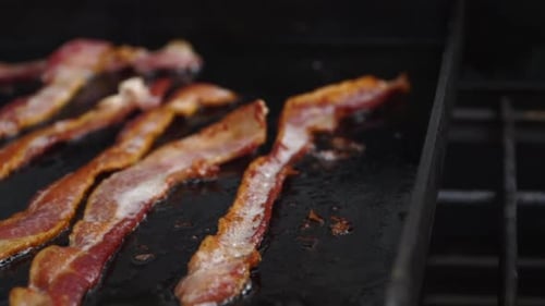 Extreme close-up, narrow focus crisp bacon sizzling on hot oily grill