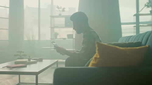 Man Using Tablet on Couch in Bright Living Room