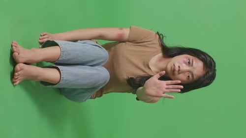 Woman With Bruise On Face Looks Into Camera Showing Hand Sign To Stop Violence On Green Screen