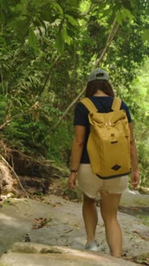 Vertical video. Young Woman Walks Along Shaded Rocky Path Next to Jungle Stream in Samui Island, Rea