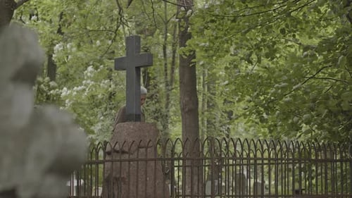 Alte asiatische Frau blickt auf das Kreuzdenkmal auf dem Friedhof