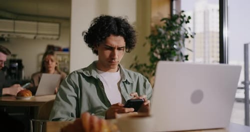 Portrait Of Hispanic Man With Smartphone Sitting In Cafe Messaging In Mobile App Shopping Online