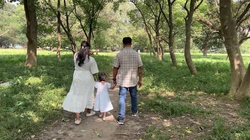 Family consisting of father, mother and daughter walking in a forest. Green foliage.