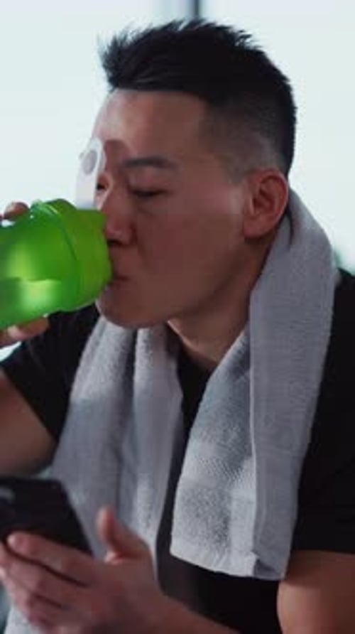 Man Drinking Protein Shake and Using Phone