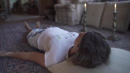 Young latin female meditating ritual with candles lying on the floor in a wooden home Slow motion an