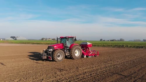 Roter Traktor pflügt an einem sonnigen, frischen Tag ein braunes Erdfeld, an dem Vogelschatten vorbeiziehen
