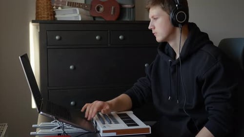 Young Man Composing Music with Keyboard and Laptop