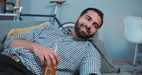 Man Lying on Sofa Relaxing with Drink and TV