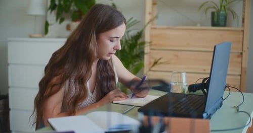 Young Woman Writing in Notebook with Laptop at Desk