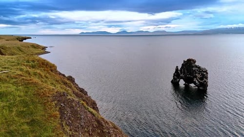 Unusually-shaped crooked black rock peeping out of water. Coast of Iceland on gloomy daytime.