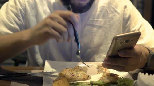 Young man texting on smartphone during evening meal in a cafe at night
