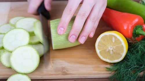 Slicing Zucchini on Wood Cutting Board with Knife
