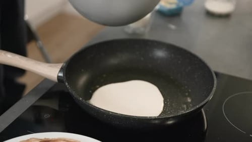Person Cooking Pancakes in Frying Pan in Kitchen