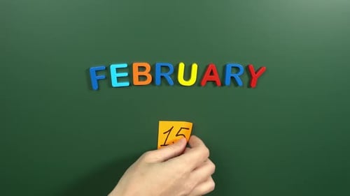 Hand sticking a sticker 15 February calendar day on school board. 15 date of February. Fifteenth