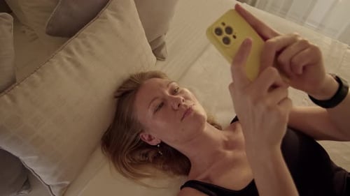 Top Down View Young Woman Lies on Bed and Use Her Cell Phone