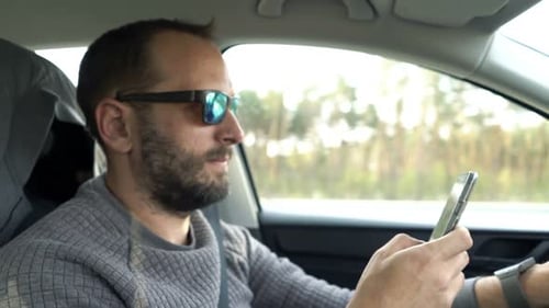 Young man texting on smartphone while driving car on a dangerous highway trip