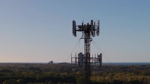 Closeup View of a Telecommunication Tower Above a Forest Landscape Near a Lake Under a Clear Blue