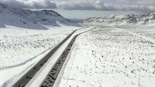 Aerial view above traffic moving along snowy mountain road scene. Icy, snowy landscape off to distan