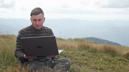 A Man Works on a Laptop in the Mountains Outdoors