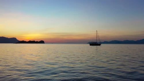 Beautiful orange sunset above the sea surface with a sail boat, sun reflection , cinematic aerial vi