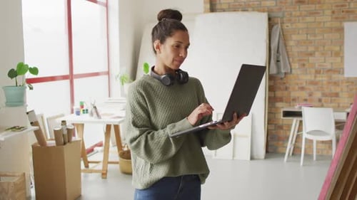 Video of happy biracial female designer using laptop in studio