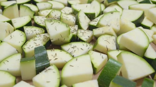 Chunks of zucchini getting seasoned with thyme. Cooking. Close up