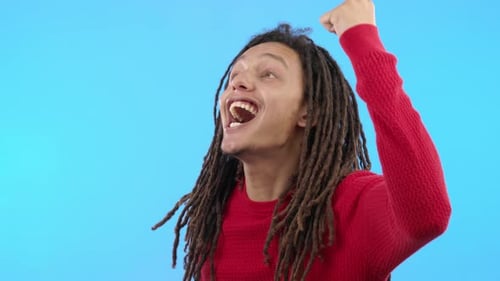 Happy, fist and man cheering, celebration and success with achievement against blue studio