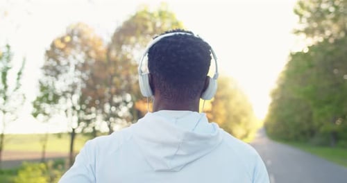 Back View of Young African American Sportsman Running Outdoors While Listening to Favorite Song in