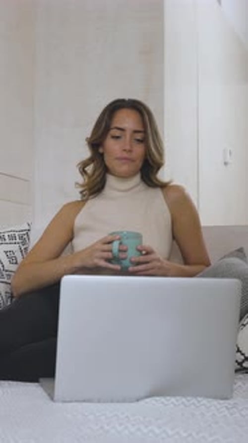 Woman Using Laptop While Drinking Coffee in Bed