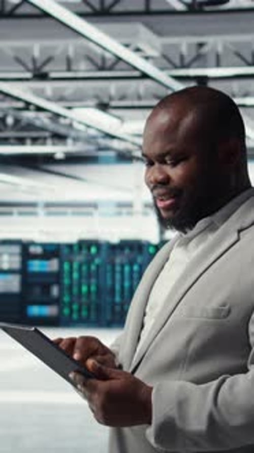 Vertical Video Engineer Working in Server Farm Using Tablet to Analyze Data